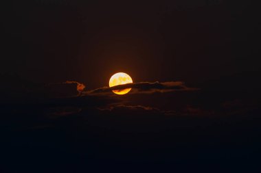 The orange moon, also known as the harvest moon or the hunter's moon, over the night sky at Sikkim, India. Moon is partly covered by clouds.