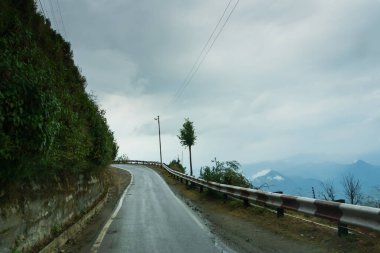 Bulutlu gökyüzü ve Himalaya yolunun kıvrımları, Garhwal muson manzarası, Uttarakhand, Hindistan. Himalayalar üzerindeki iklim değişikliği etkisi toprak kayması, zamansız yağmur ve dağ çevresinin tahrip edilmesine yol açıyor.