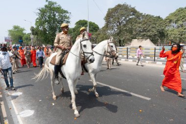 Haridwar, Uttarakhand, India - 16th April 2021 : Maha Kumbhmela event. Sadhu in saffron dress shooting police guards on horses leading sadhus procession on road for shahi snaan on river Ganges. clipart