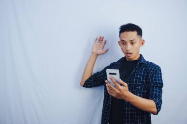 Yakışıklı Asyalı adam, beyaz arka planda okunmuş ticaret ve sohbet sonrasında cep telefonu ekranına şaşırmış görünüyor.