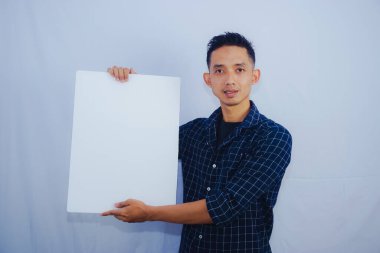  Reklam Kavramı. Beyaz stüdyo arka planında boş tahta tutan Asyalı adamın portresi. İlan için beyaz kare kağıt pankartlı bir adam duruyor, kameraya gösteriyor.