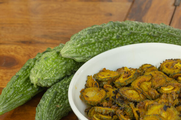 Fresh green organic Bitter gaud vegetable kept along with cooked bitter gaud on a wooden table with copy space