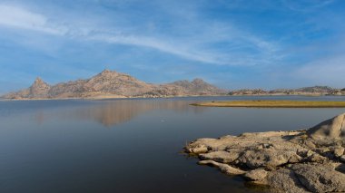 Arka planda tepeler ve bulutlar olan el değmemiş Jawai Barajı manzarası 
