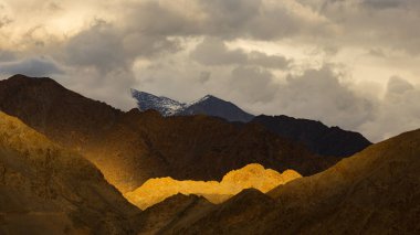 Dağların siluetinin dramatik bir görüntüsü. Güneş ışınları bulutlarla birlikte düşüyor.