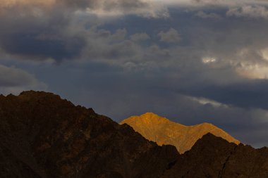 Dağların siluetinin dramatik bir görüntüsü. Güneş ışınları bulutlarla birlikte düşüyor.