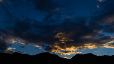 Dağların siluetinin dramatik bir görüntüsü ve bulutların üzerine düşen güneş ışınları. 