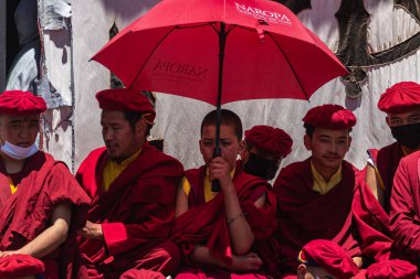 Tibetli keşişler, 5 Temmuz 2024 'te Leh, Hindistan' da birlikte oturan kırmızı cüppeli ve şemsiyeli rahipler..