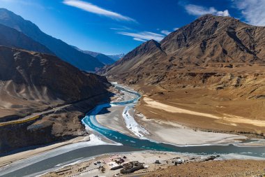 Sangam 'da Indus nehri ve Zanskar nehrinin birleşiminin panoramik görüntüsü. Arka planda dağlar, gökyüzü ve bulutlar var..