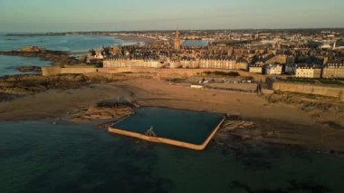 Güçlendirilmiş ortaçağ kasabası Saint-Malo 'nun hava manzarası günbatımında tarihi surlarını ve okyanuslarla beslenen havuzunu sergiliyor. Canlı günbatımı renkleri suyu yansıtıyor ve dingin bir ortam yaratıyor..