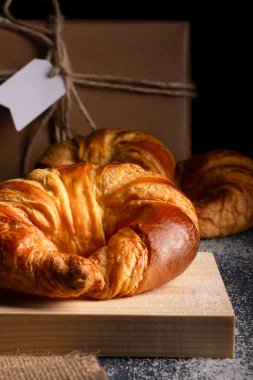 Koyu bir tezgahın üzerine koyulmuş sulu kruvasanlar en alttaki kaba ambalajlı pakette.