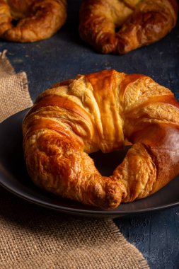 Çuval bezi üzerinde siyah bir tabağa yerleştirilmiş iştah açıcı bir kruvasanın yakın plan fotoğrafı..