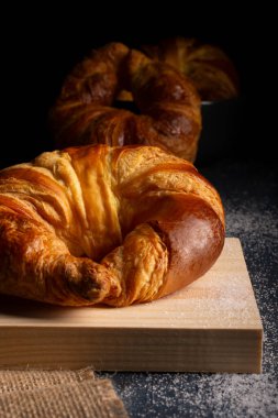 Tahta bir tahtaya yerleştirilmiş sulu kruvasan çuval bezi. Kruvasan ile koyu arkaplan