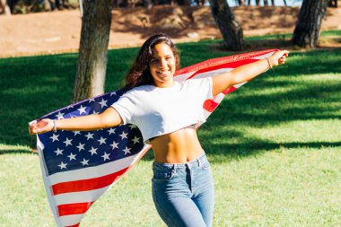 Arkasında açık Amerikan bayrağı olan gülümseyen Amerikalı Latin kız. Odaklanma arkaplanı.