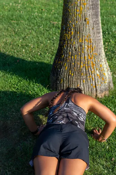 Spor kıyafetleri ve saçlarında örgülerle çimlerin üzerinde şınav çeken bir kız. Çimen arkaplanı.