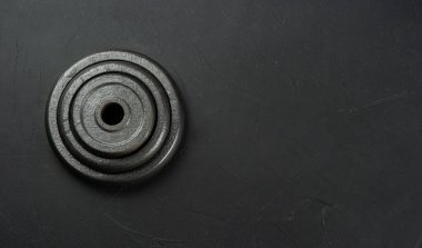 Metal pancakes from dumbbells in a heap on an empty dark background. copy space, top view.