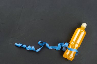 Orange isotonic for drinking in a plastic bottle with a measuring tape on an empty dark concrete background. copy space, top view.