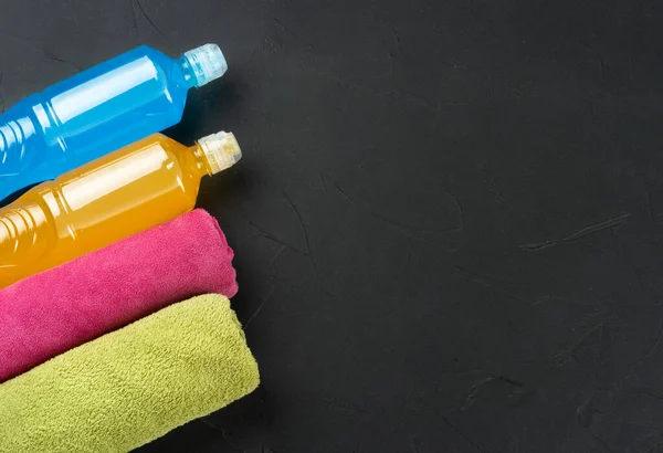 Blue and orange isotonic drink for sports with two towels on a dark concrete background, copy space.