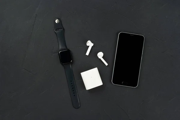 Fashion gadgets, mobile phone, smart watch and wireless headphones on a dark concrete background, top view.