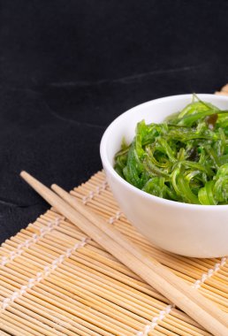 Chuka deniz yosunu salatası beyaz bir tabakta ve Çin yemek çubukları yakın planda.