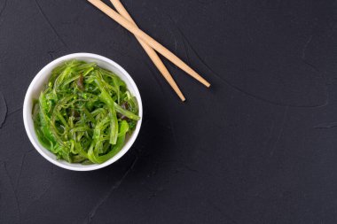 Chuka deniz yosunu salatası ve siyah bir arka planda yemek çubukları.