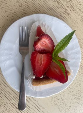   Çilek reçelli cheesecake ve taze çilekle süslenmiş beyaz bir tabakta kesilmiş ve nane şekeri ile çatallı tatlı.