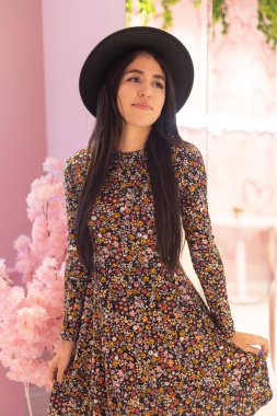 Uzun düz saçlı, latin ince kadın, aksesuar ve elbise olarak siyah şapkalı, moda ve doğal güzellik, stüdyoda pembe arka planda.