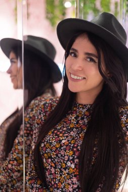 Kameraya bakan ve gülümseyen genç bir kadının yüzü, bir şapka ve elbise giyerek moda, aynada yansıması olan doğal güzellik.