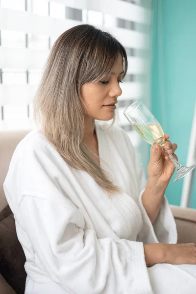 joyful luxurious relaxed lifestyle, beautiful young woman holding drink in glass, wearing comfortable bathrobe while resting, natural beauty