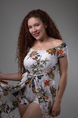 posing standing latin woman with long curly hair, wears makeup with red lips and wears a patterned dress, beauty and casual fashion