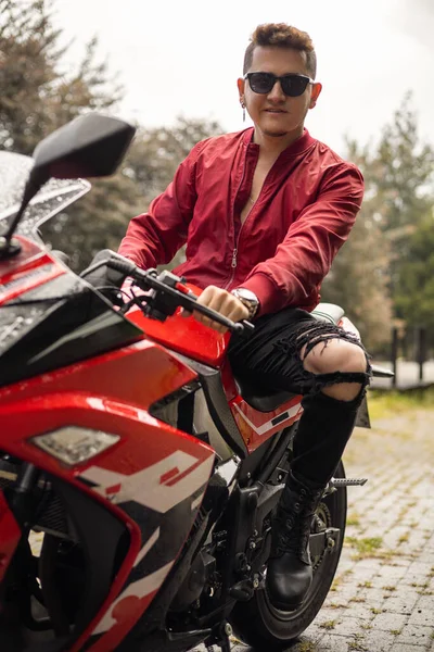 stock image posing on a sports motorcycle a young man who has short hair and wears sunglasses, casual jacket, adventurous lifestyle, fashion and means of transportation