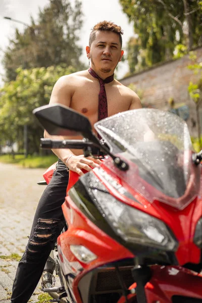 Latin young man without a shirt and with a tie sitting on a motorcycle, urban lifestyle, transport and adventure