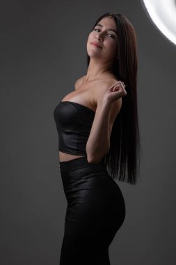 Uzun siyah saçlı, doğal makyajlı genç bir Latin kadın modern bir bluz ve etek giyiyor. Stüdyoda poz veriyor.