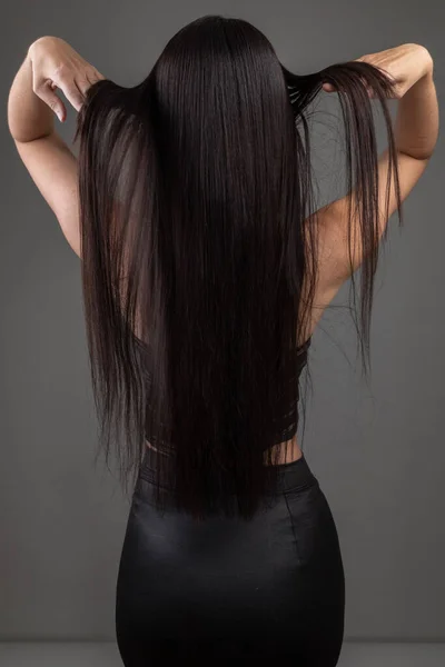 背中には若い女性の長い黒のストレートシルキーな髪の質感 スタジオでは人のシルエット サロンヘアケア — ストック写真