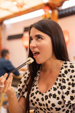 Lokantada yemek çubuklarıyla hamur köftesi yemek, siyah düz saçlı genç bir kadının yaşam tarzı, geleneksel Asya yemekleri, kadın mankeni