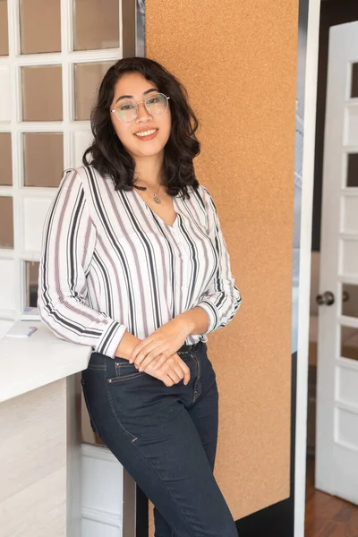 young model standing at the reception of an office, young latin woman with short wavy hair wears glasses and elegant blouse, beauty and youth fashion