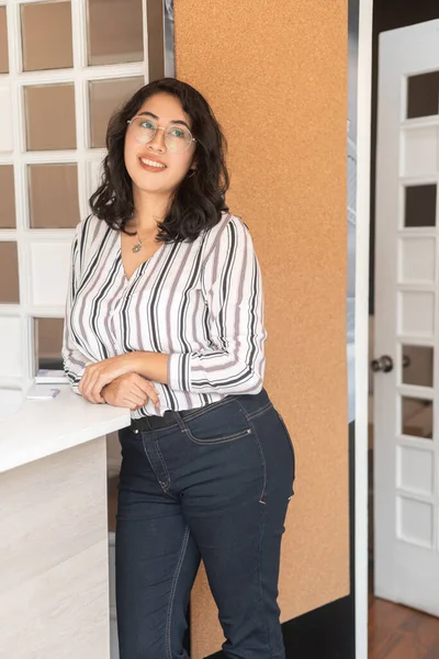 posing at the reception of an office, young latin woman with short wavy hair wears glasses and elegant blouse, beauty and casual fashion, lifestyle