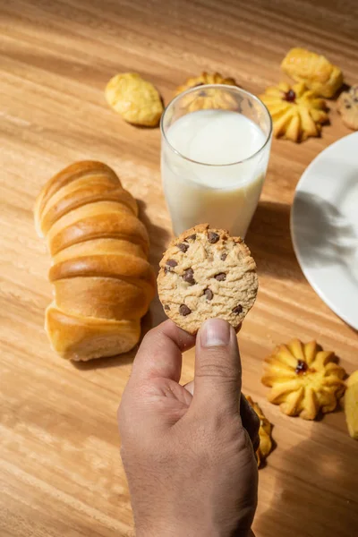 holding a sweet cookie to eat, table served with cookies with chocolate, glass of milk and bread, pastry table, wallpaper