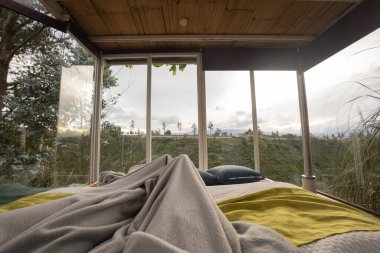 Rahat ve rahat bir yaşam tarzı, battaniyeli bir yatak odası arka planda bitkiler olan büyük pencereli bir yatak odası, tatil için turistik bir yer.