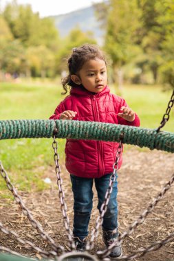 Güneşli bir gün, salıncakta sallanan küçük bir Latin kız, günlük kıyafetlerle parkta eğleniyor, çocuklar ve yaşam tarzı, mutlu bir insanın portresi.