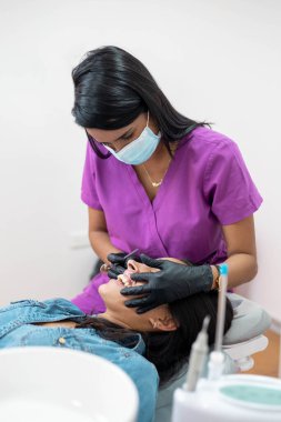 Genç bir hastaya teşhis koyan siyah saçlı genç bir kadın. Ağız sağlığı, diş hekimi, iş yeri, mesleği.