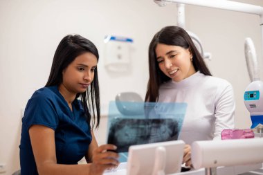 Diş hekimi, hastasıyla birlikte sağlık muayenehanesinde x-ray testlerini inceliyor. Profesyonel meslek ve hastalık önleme, yaşam tarzı.