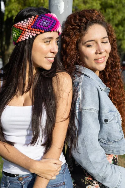 in a park two sisters playing and enjoying, one with curly hair and the other with straight hair and a headband, smiles and leisure, natural beauty and family love