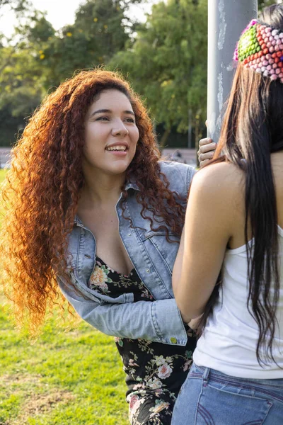 beauty of latin women with curly hair and another with straight hair and a colorful headband, youth fashion in a park with nature, lifestyle