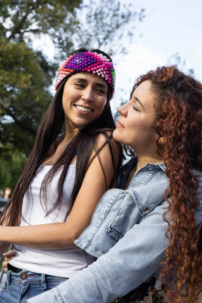 latin women with curly hair and another with straight hair and a colorful headband, smiles and leisure in a park, natural beauty and youth fashion, lifestyle