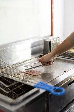 Yemek pişiren bir çalışanın elleri, fast food için taze malzemeler, ızgara ve tavalı mutfak aletleri.