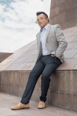 Zarif iş adamı açık mavi gömlekli bir takım elbise giyiyor. Aksesuar olarak güneş gözlüğü takıyor. Lüks bir manken.