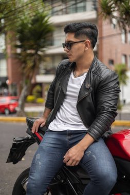 Güneşli bir günde motosikletçi, rahat bir hayat tarzı, deri ceket giyen genç bir Latin 'in portresi, gençlik ulaşım aracı, şehir