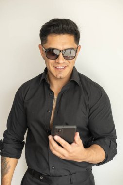 Çekici genç adam cep telefonu kullanıyor, siyah takım elbise ve güneş gözlüğü takıyor, şehir yaşam tarzı, iş adamı çalışıyor ve iletişim kuruyor.