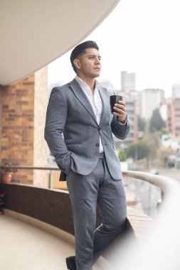 Bir fincan kahvenin keyfini çıkarırken gri takım elbiseli ve gömlekli genç bir adam işe ara veriyor, insan portresi, moda...