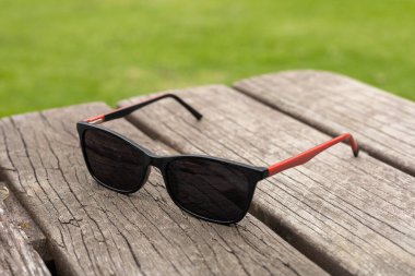 Ahşap bir masada dinlenen siyah güneş gözlükleri. Gözlüklerin parlak siyah dizaynı ile ahşabın doğal dokusu arasındaki zıtlık 